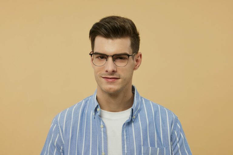 A man wearing glasses standing in front of a wall
